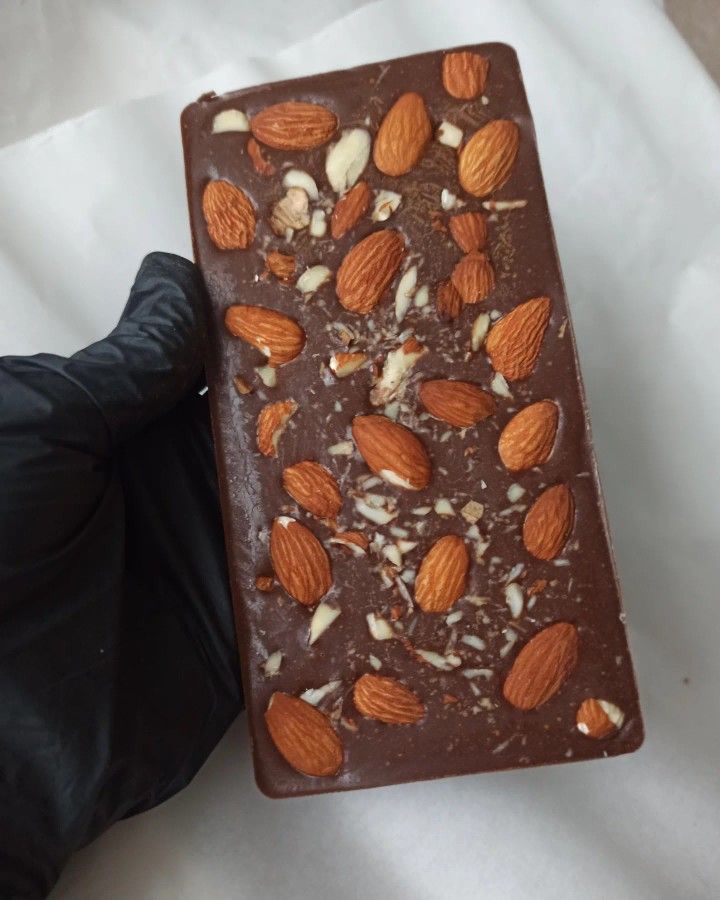 a chocolate bar topped with almonds on top of a white table cloth and black gloves