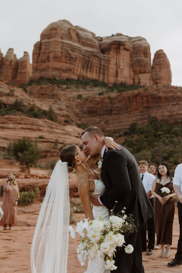 a bride and groom kissing in front of the red rocks