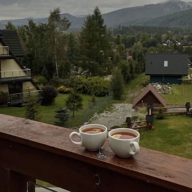 two cups of coffee sitting on top of a wooden table in front of some houses