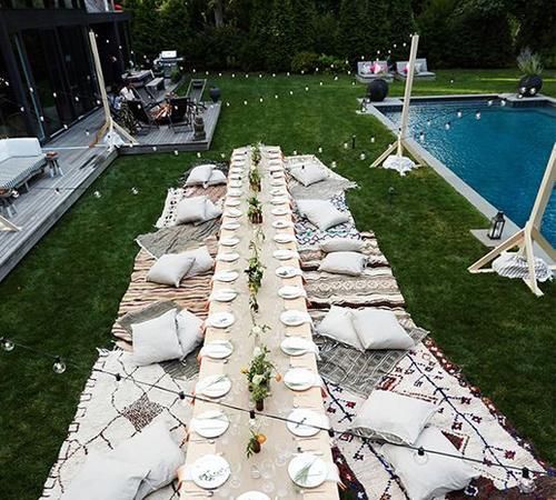 a long table is set up with white plates and place settings for dinner by the pool