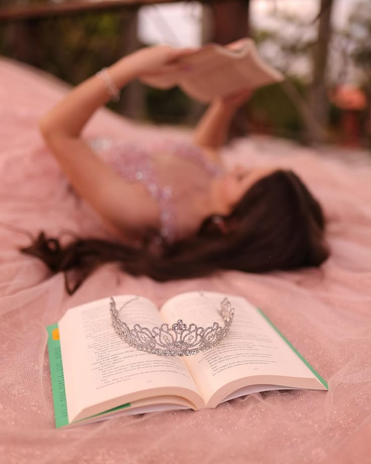 a woman laying on top of a bed reading a book and wearing a tiara