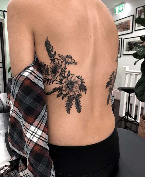 the back of a woman's body with flowers tattooed on her left shoulder and chest