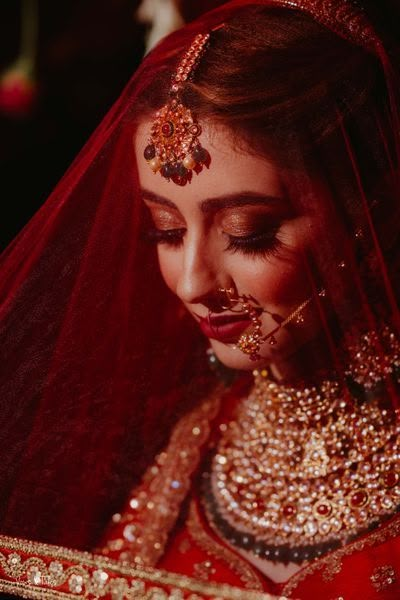 a woman wearing a red and gold bridal outfit with her veil pulled back in the wind