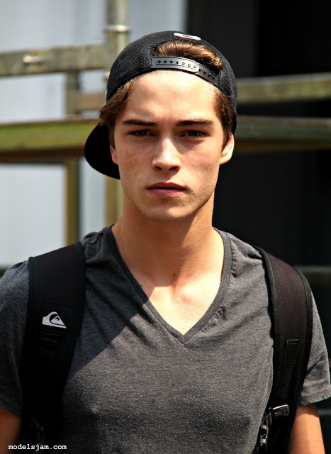 a young man wearing a black hat and carrying a backpack in front of a building