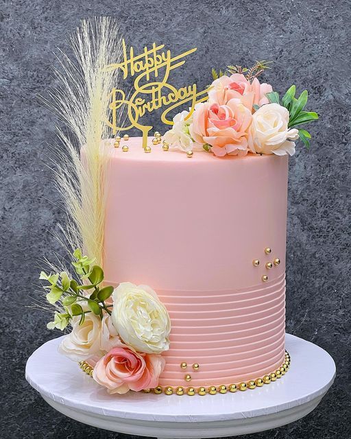 a pink and gold birthday cake with flowers on top