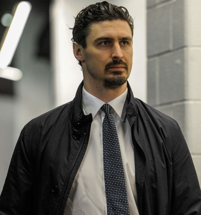 a man wearing a suit and tie standing in front of a brick wall