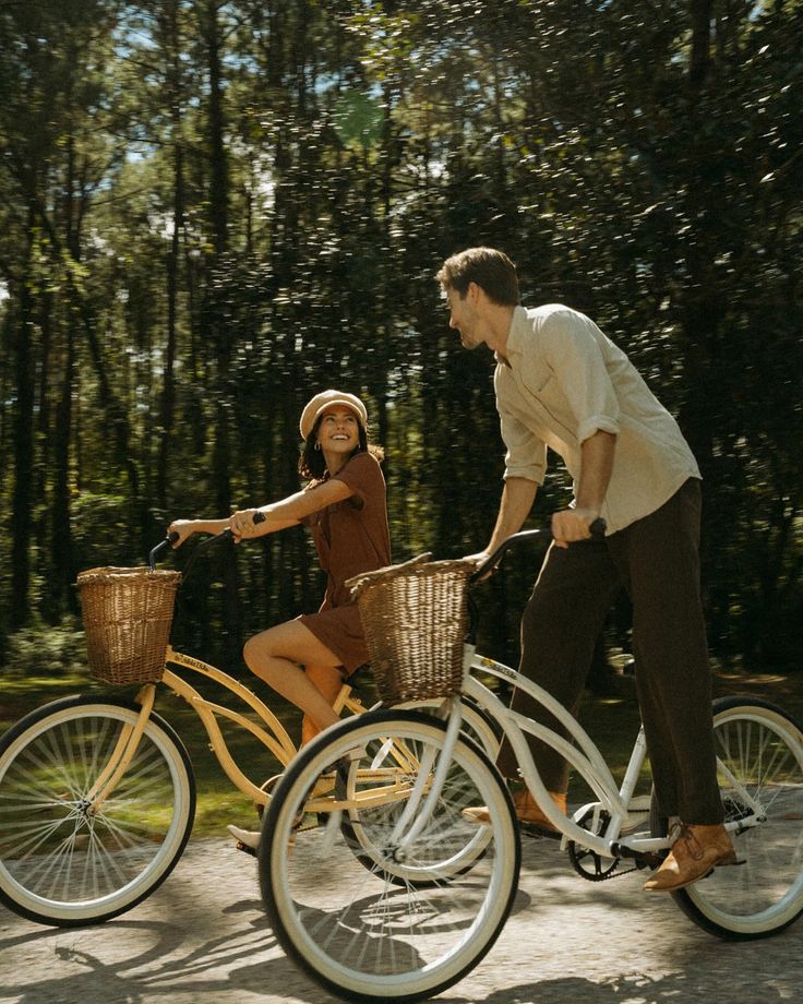 a man and woman riding bikes in the woods together, with baskets on the handlebars