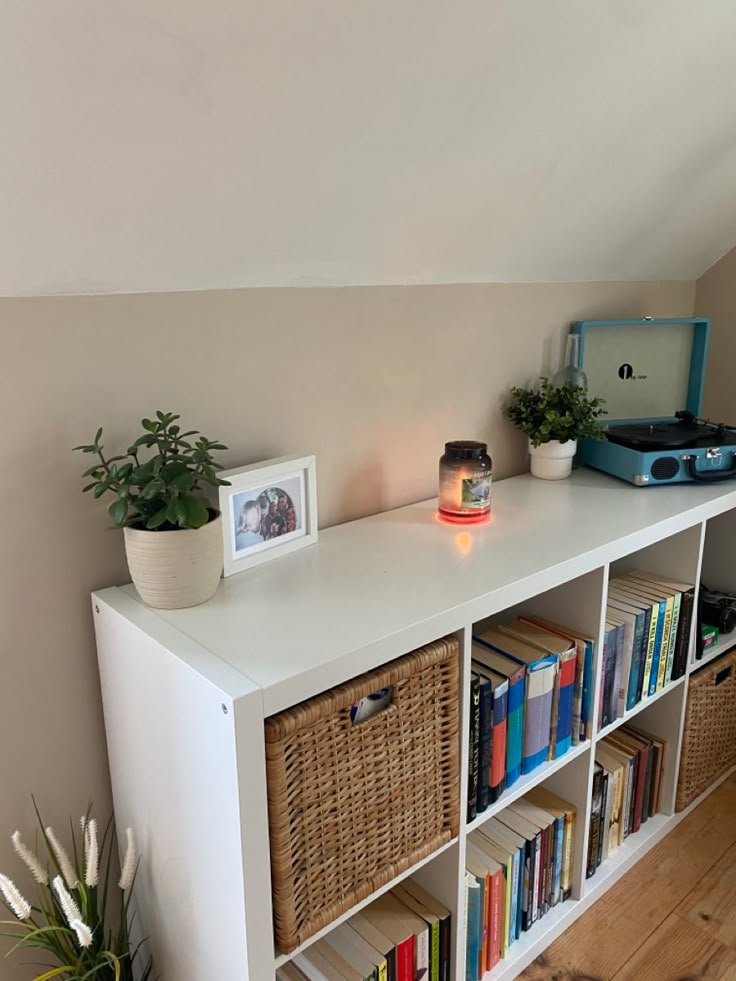 a white book shelf with baskets and books on it next to a wall mounted record player