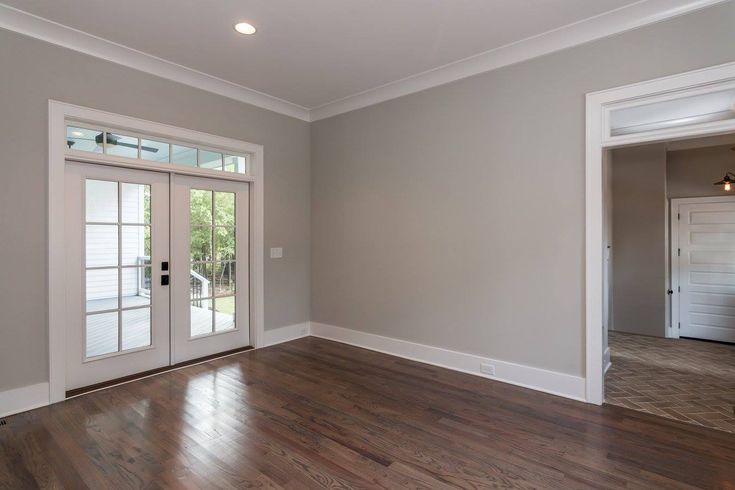 an empty living room with wood floors and white trim on the doors, windows, and french doors