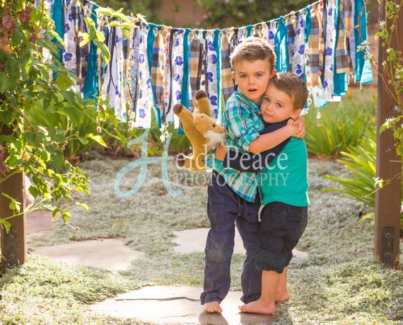 two young boys hugging each other in front of an arch with clothes hanging from it