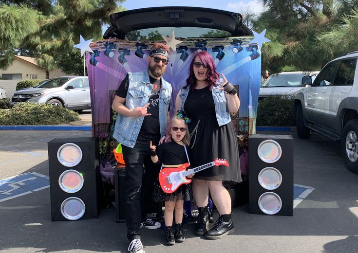 two adults and a child standing in front of a car with an electric guitar on display