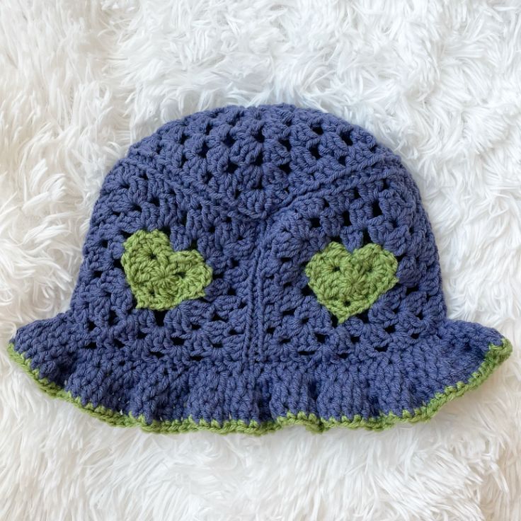 a crocheted blue hat with green hearts on the side sitting on a white furnishing