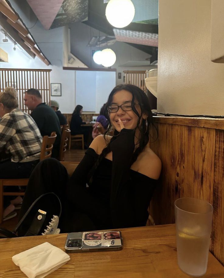 a woman sitting at a table with her hand on her face, smiling for the camera