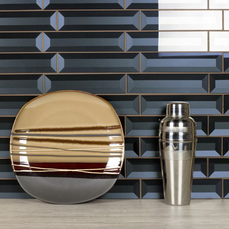 an empty plate next to a metal cup and shaker on a counter with geometric tiles in the background