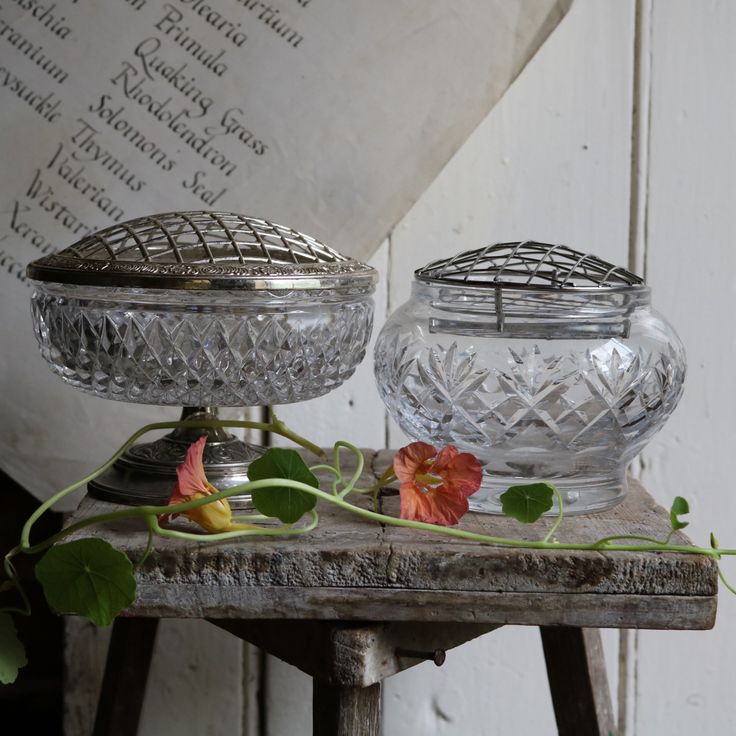 two glass dishes sitting on top of a wooden table next to a flower and leaves