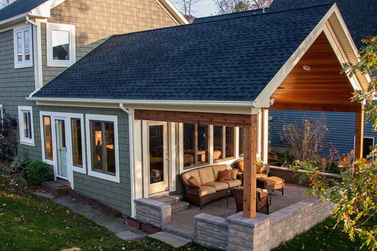 an outdoor living area with couches and chairs in front of a gray house on a sunny day