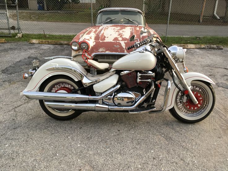 a motorcycle parked next to an old car in a parking lot near a chain link fence