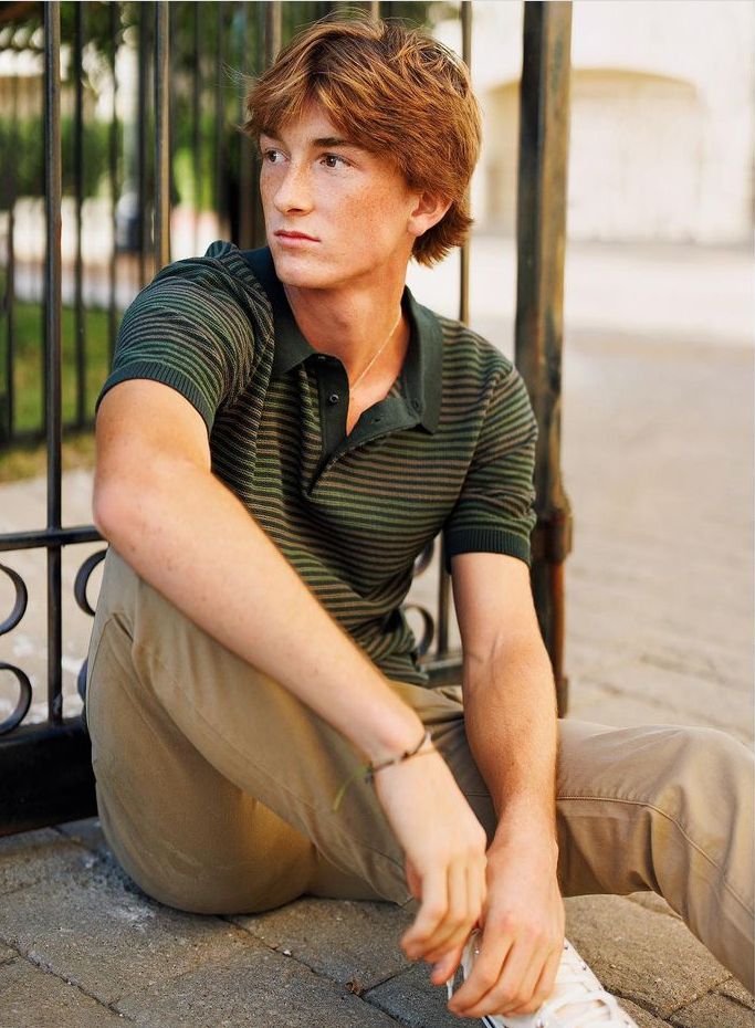 a young man sitting on the ground next to a black iron fence with his foot propped up