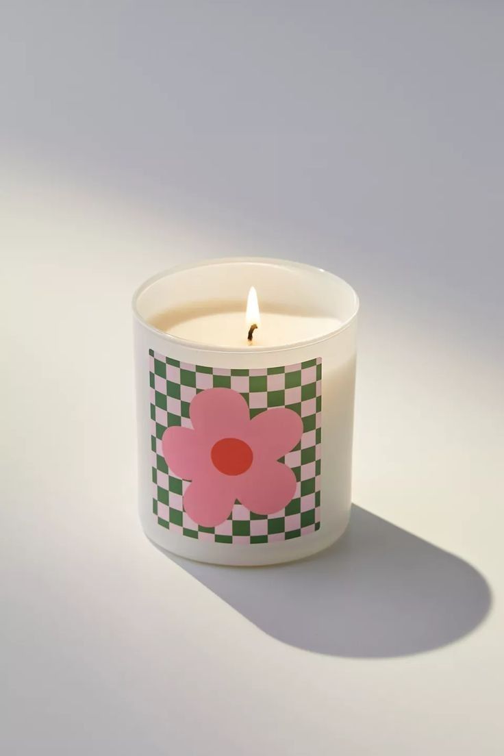 a white candle with a pink flower on the front and green checkerboard around it