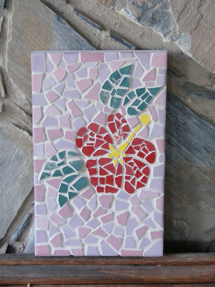 a mosaic tile with flowers on it sitting on top of a wooden shelf next to a stone wall