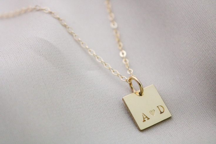 This delicate Tiny Square Initial Necklace is the perfect way to celebrate your unique bond. Crafted with the highest quality sterling silver or gold filled material, this couples necklace can be personalized with two initials for an extra special touch. A timeless anniversary gift, it's perfect for expressing your love. Tickle Bug Jewelry is made to live life along with you, so whether you're sleeping or swimming, you don't have to take it off! The square pendant measures a dainty 1/2" size, and fits up to two initials with your choice of a +, & or heart in between! Available in either 14K Gold Filled or .925 Sterling Silver Includes one 1/2" square pendant Fits up to 3 characters ( initial symbol initial) Uppercase or Lowercase Typewriter font available Delicate adjustable length cable c Silver 14k Gold Name Necklace For Anniversary, Customizable 14k Gold Necklaces For Anniversary Gift, 14k Gold Name Necklace For Anniversary, Elegant Nameplate Initial Necklace For Anniversary, Elegant Name Necklaces For Anniversary Gift, Classic Pendant Initial Necklace As A Gift, Elegant Custom Name Necklace For Anniversary, Elegant Personalized Necklace For Anniversary Gift, Classic Square Pendant Jewelry As Gift