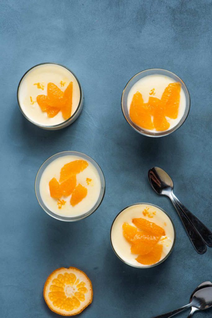 four glasses filled with yogurt and orange slices