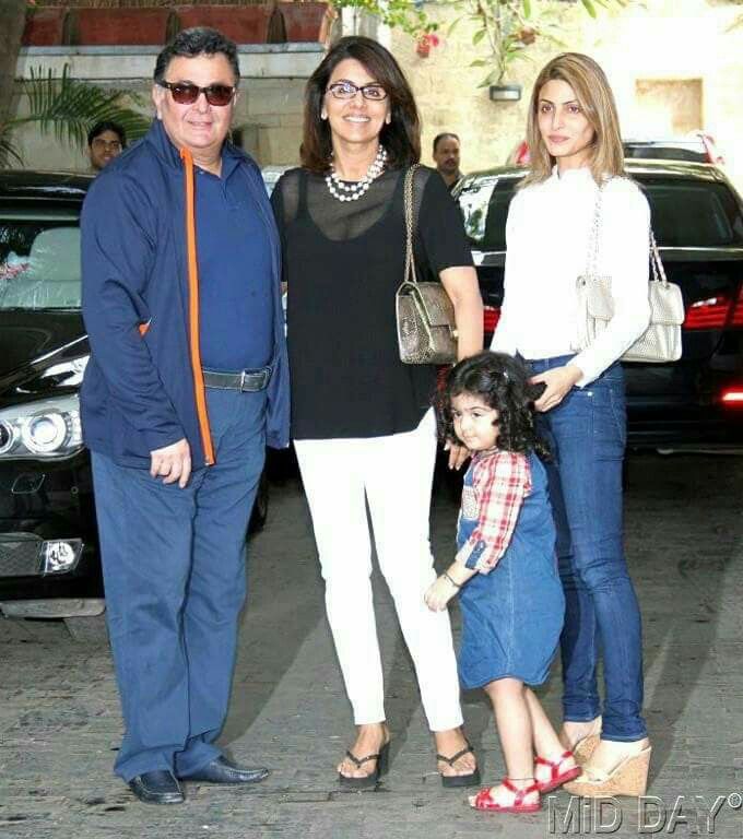 three people standing next to each other in front of a car with two women and one man