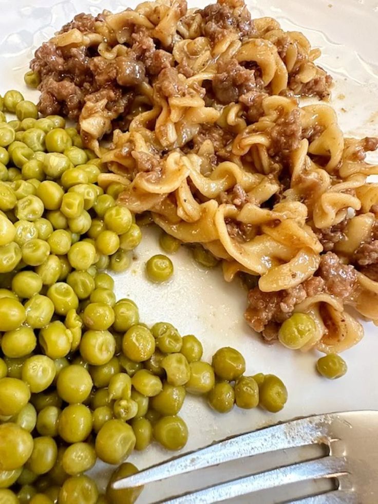 some green beans and pasta on a white plate with silver utensils next to it