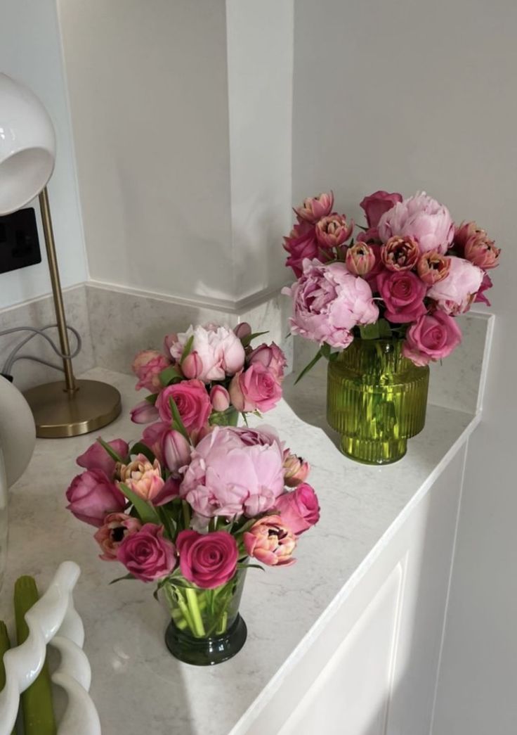 two vases filled with pink flowers sit on a white counter next to a lamp