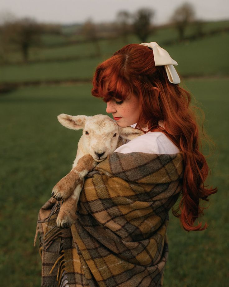 a woman with red hair is holding a lamb in her arms and looking at the camera