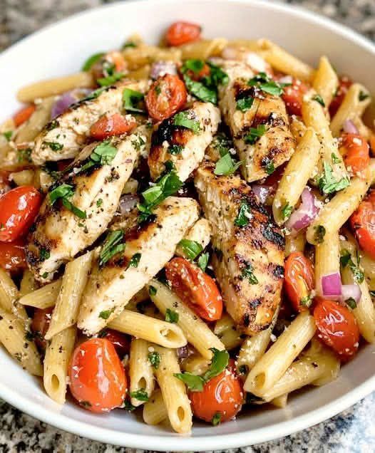 a white bowl filled with pasta and chicken covered in tomatoes, onions, and parsley