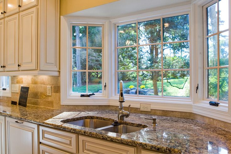 a kitchen with marble counter tops and white cabinets, two large windows above the sink