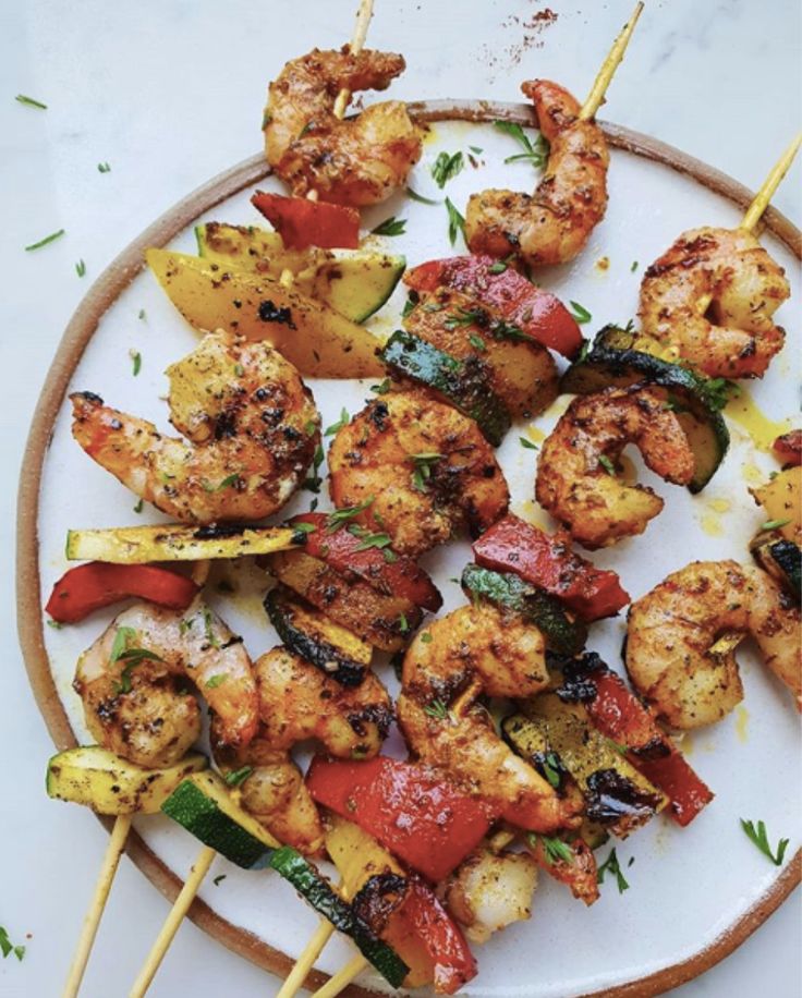 grilled shrimp and vegetable skewers on a white plate with wooden skewers