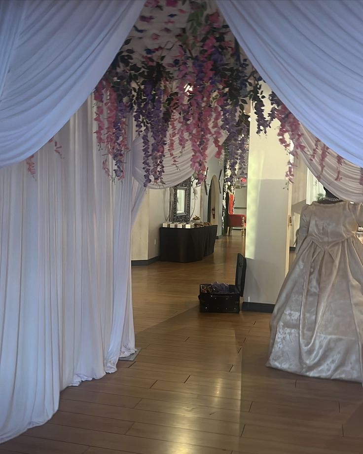 a room with white drapes and purple flowers hanging from the ceiling in front of it