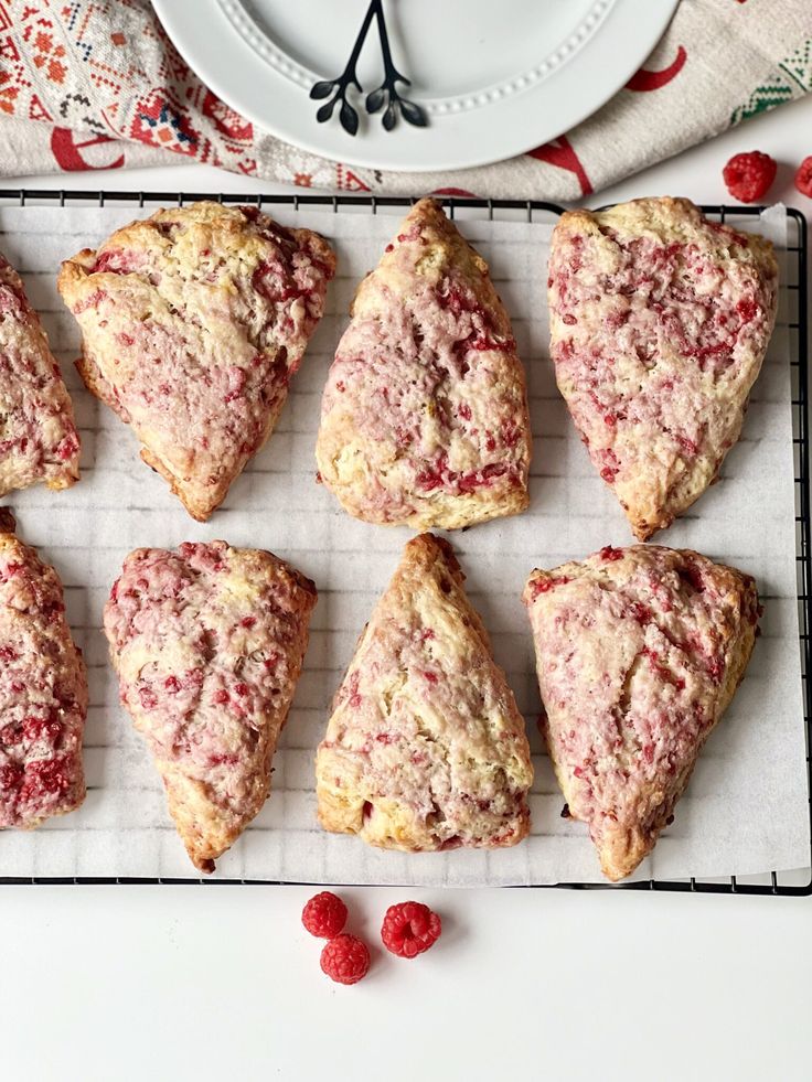 nine raspberry scones sitting on a cooling rack next to a white plate