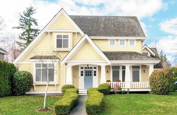 a yellow house with hedges in front of it and trees on the other side of the house