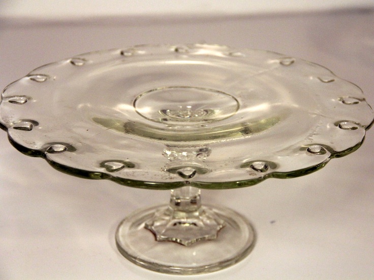 a clear glass cake plate sitting on top of a white tableclothed countertop