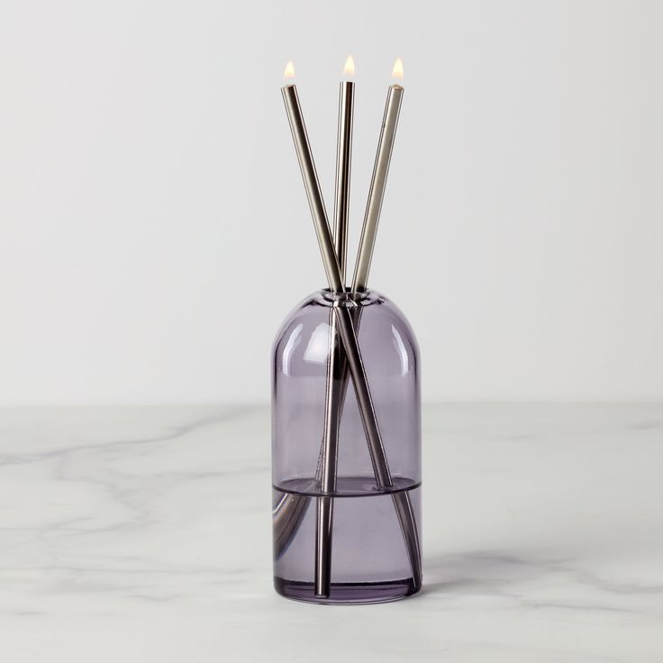 three candles in a purple glass vase on a marble surface