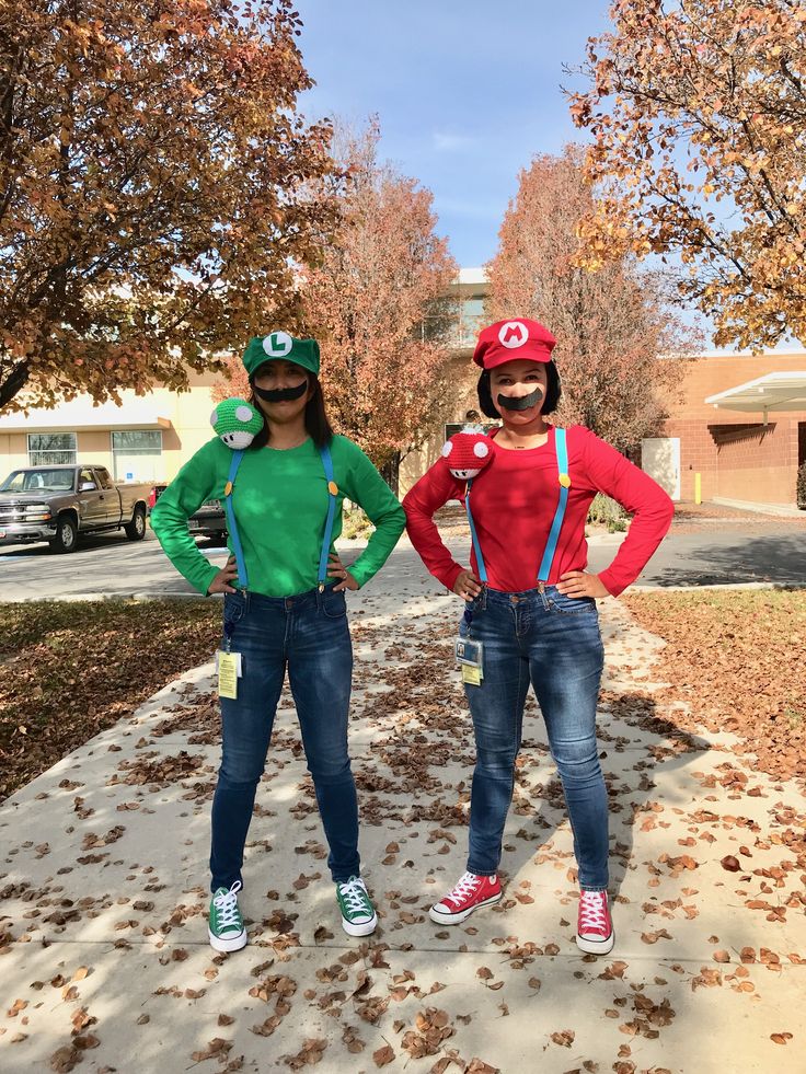 two people dressed up as mario and luigi from mario bros standing on a sidewalk with their hands on their hipss