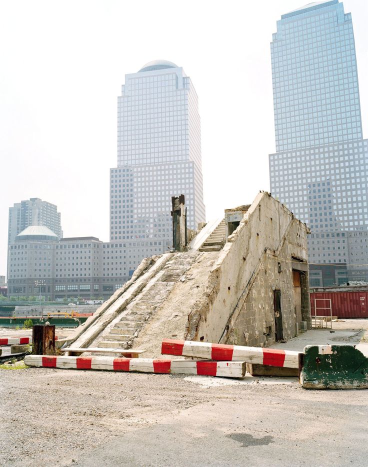 an abandoned building in front of some very tall buildings with red and white striped barriers