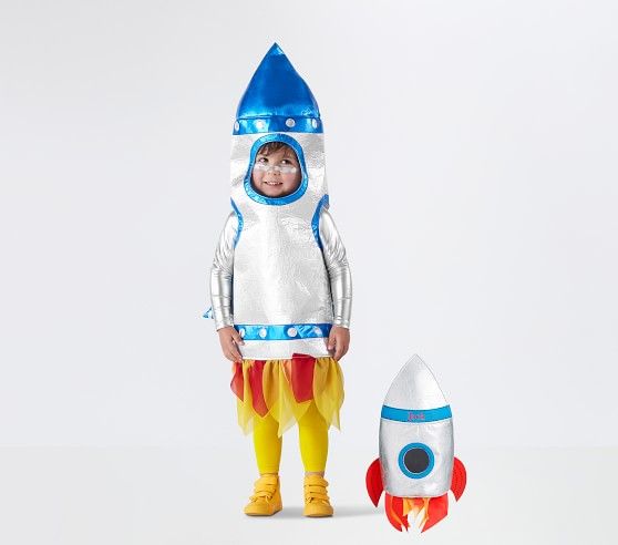 a little boy in a space suit standing next to a toy rocket ship on a white surface