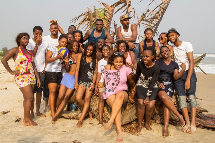 a group of people standing on top of a sandy beach next to the ocean in front of a tree