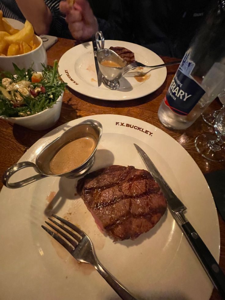 two plates with steak, french fries and salad on the side at a restaurant table