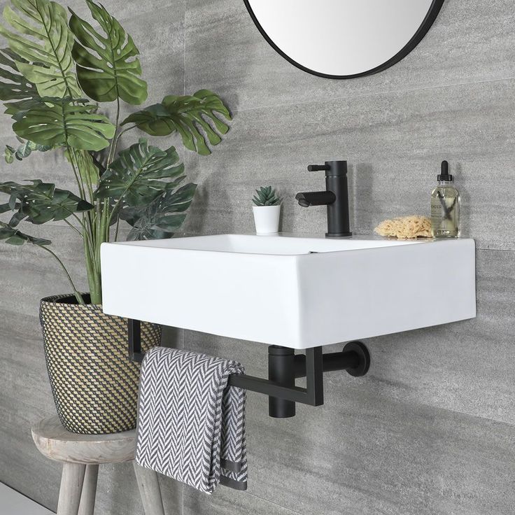 a white sink sitting under a mirror next to a potted plant