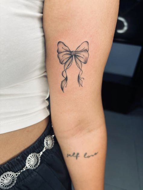 a woman's arm with a bow tattoo on the left side of her body