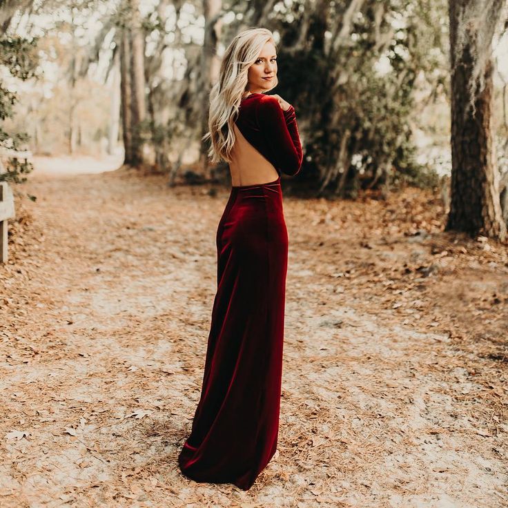 a woman standing in the woods wearing a red velvet dress and looking off into the distance