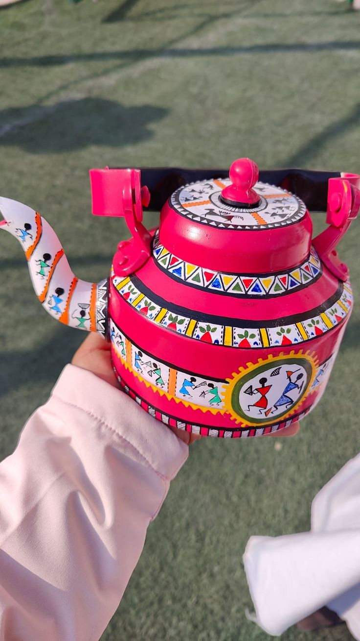 a hand holding a colorful tea kettle with designs on it