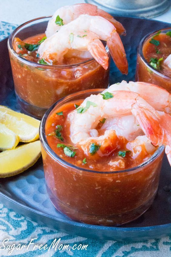 three glasses filled with shrimp and sauce on a blue plate next to lemon wedges