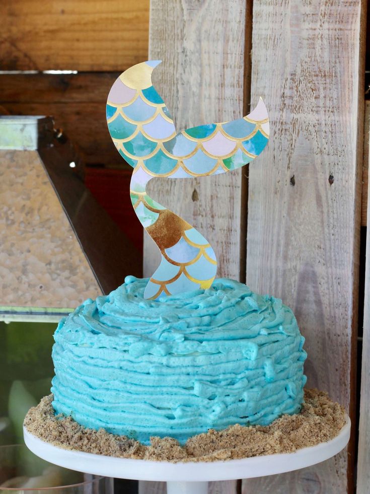 a cake with blue frosting and a gold fish on top sitting on a table