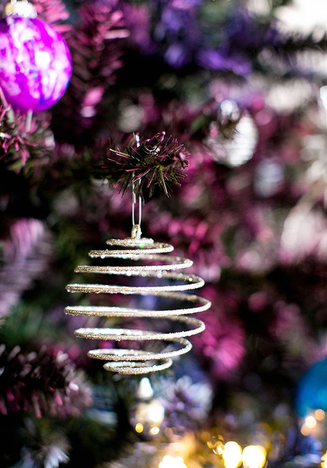 an ornament hanging from a christmas tree in front of purple and gold ornaments